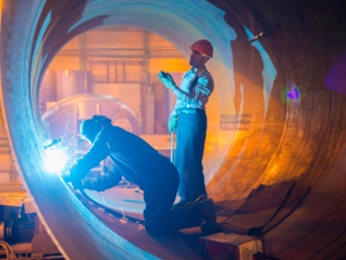 Two male welders working on metal pipe