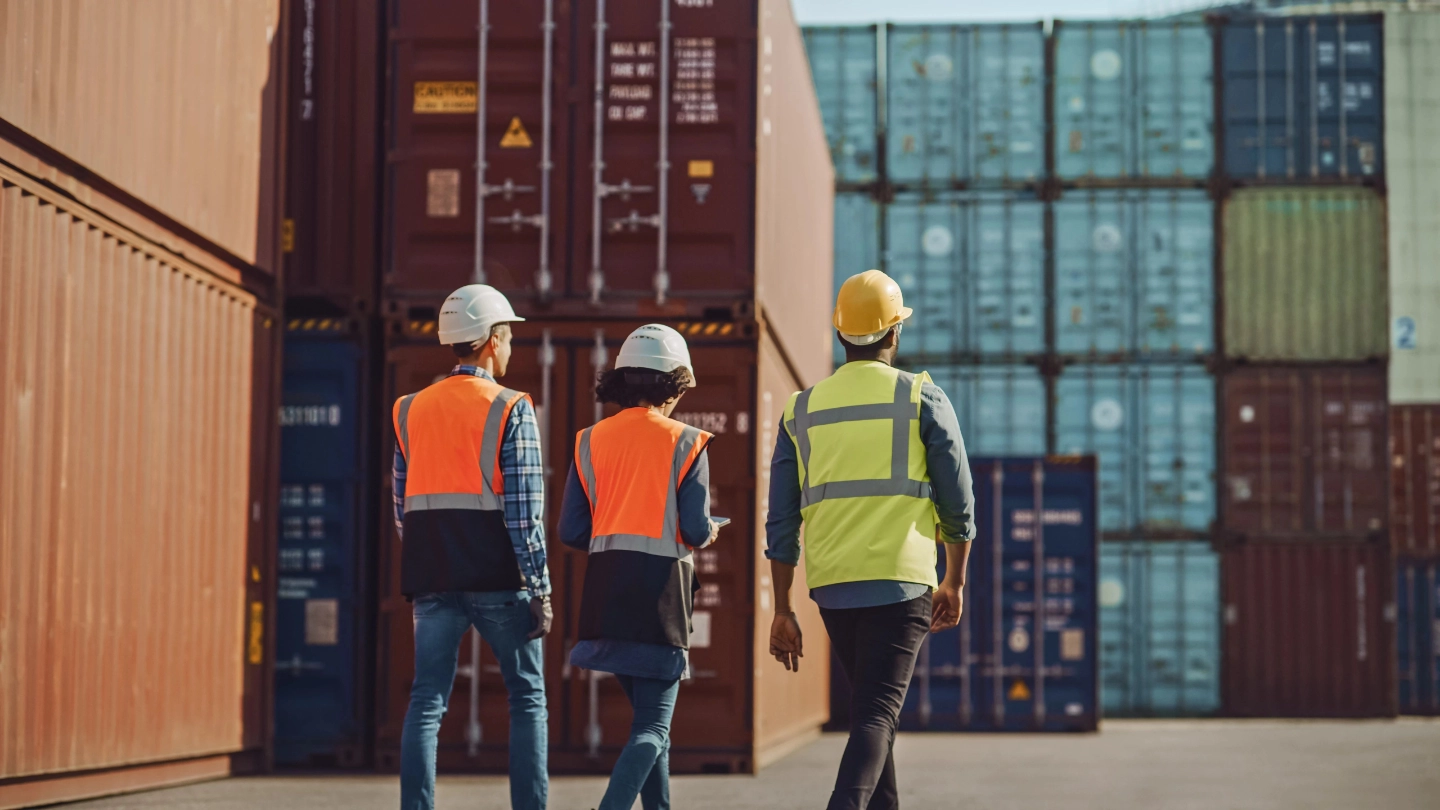 two men and woman walking in a shipping container yard (1) image